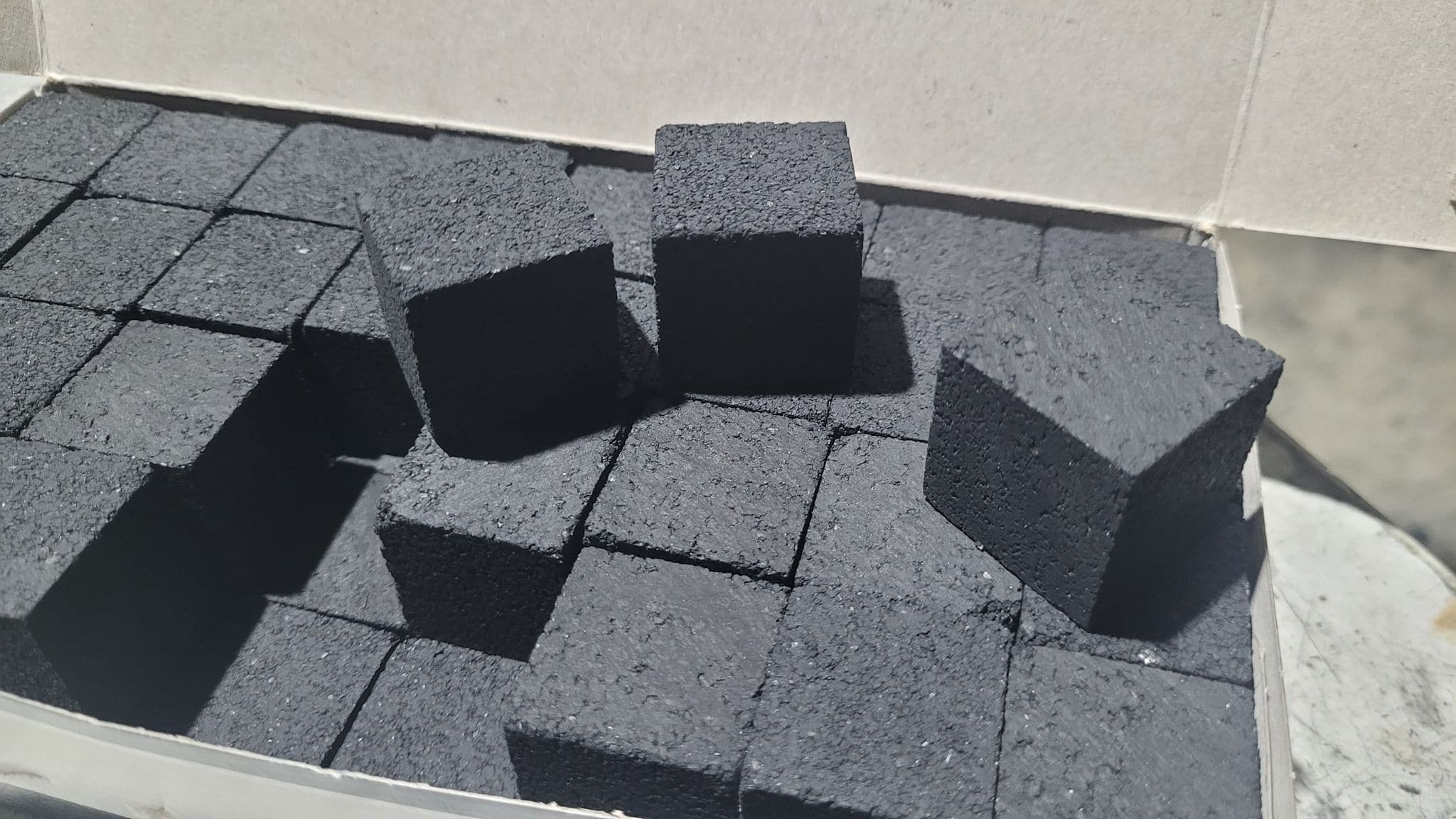Matte black charcoal cubes with a porous texture stacked inside a white box.